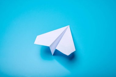Pastel mavi zemin üzerine beyaz kağıt origami uçak yatıyor