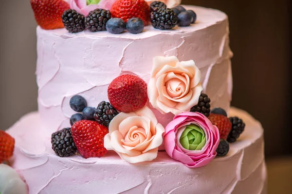 三层粉红色的婚礼蛋糕, 上面点缀着浆果和花朵。糖胶糕点植物区系的概念 — 图库照片