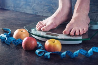 Kadın ayakları koyu arka plan üzerinde kilo kontrolü için elektronik teraziler tutuyoruz. Spor eğitim, beslenme kavramı