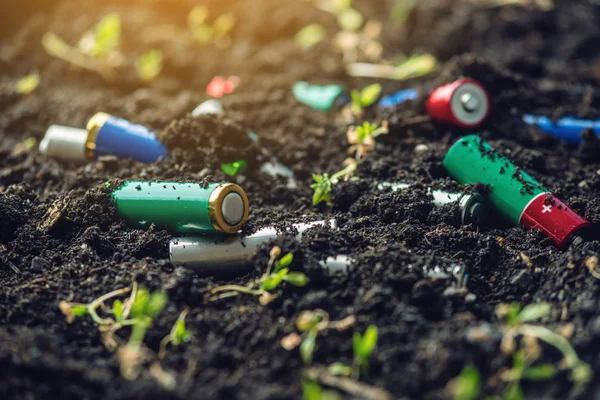 Las baterías alcalinas usadas se encuentran en el suelo donde crecen las plantas. Concepto de contaminación ambiental con residuos domésticos tóxicos —  Fotos de Stock