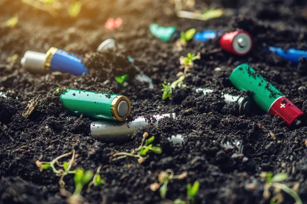 Las baterías alcalinas usadas se encuentran en el suelo donde crecen las plantas. Concepto de contaminación ambiental con residuos domésticos tóxicos —  Fotos de Stock