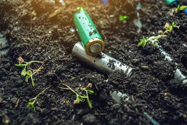 Las baterías alcalinas usadas se encuentran en el suelo donde crecen las plantas. Concepto de contaminación ambiental con residuos domésticos tóxicos —  Fotos de Stock