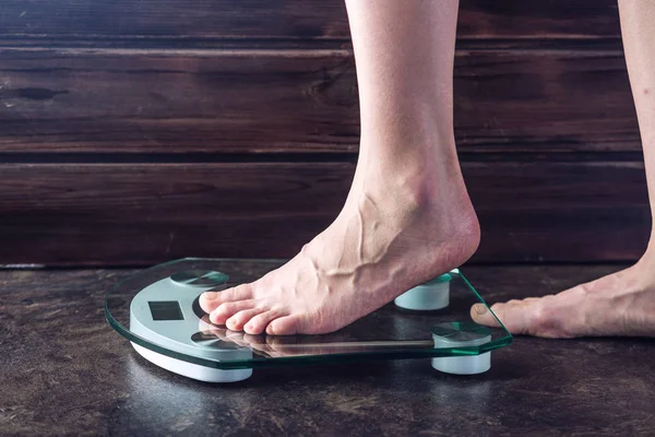 Female feet standing on electronic scales for weight control on dark background. Concept of sports training, diets