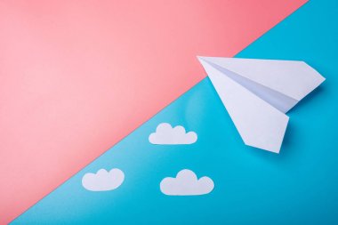 Beyaz kağıt origami uçak bulutlar ile pastel mavi arka plan üzerinde üstten görünüm yatıyor.