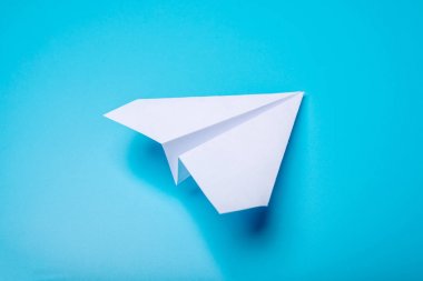 Beyaz kağıt origami uçak pastel mavi arka plan üzerinde üstten görünüm yatıyor.