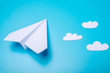 Beyaz kağıt origami uçak pastel mavi arka plan üzerinde üstten görünüm yatıyor.