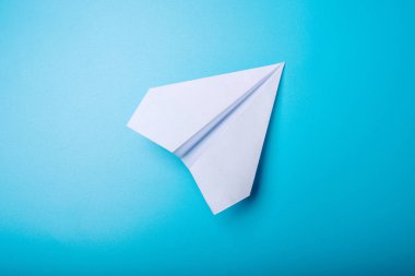 Beyaz kağıt origami uçak pastel mavi arka plan üzerinde üstten görünüm yatıyor.