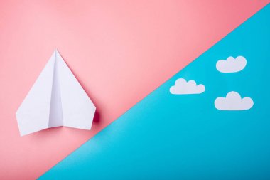 Beyaz kağıt origami uçak bulutlar ile pastel mavi arka plan üzerinde üstten görünüm yatıyor.