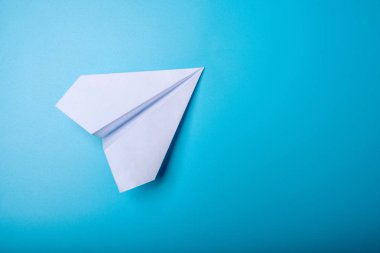 Beyaz kağıt origami uçak pastel mavi arka plan üzerinde üstten görünüm yatıyor.