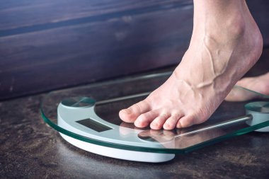 Kadın ayakları koyu arka plan üzerinde kilo kontrolü için elektronik teraziler tutuyoruz. Spor eğitim, beslenme ve kilo kaybı kavramı