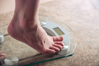 Kadın ayakları elektronik ayakta ölçekler ışık arka plan üzerinde kilo kontrolü için. Spor eğitim, beslenme ve kilo kaybı kavramı