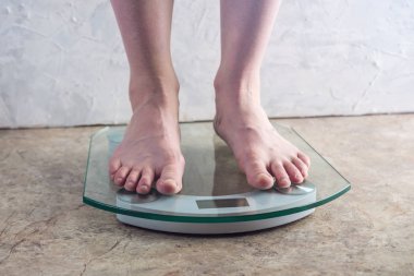 Kadın ayakları elektronik ayakta ölçekler ışık arka plan üzerinde kilo kontrolü için. Spor eğitim, beslenme ve kilo kaybı kavramı