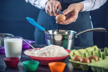 Şef pasta kek malzemelerle koyu arka plan üzerinde yapma sürecinde siyah bir önlük. Şekerleme yemek kavramı