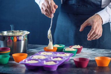 Şef pasta cupcake silikon kalıp koyu arka plan üzerinde içine hamur doldurarak bir siyah önlük. Şekerleme yemek kavramı