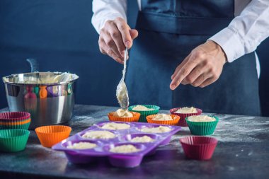 Şef pasta cupcake silikon kalıp koyu arka plan üzerinde içine hamur doldurarak bir siyah önlük. Şekerleme yemek kavramı