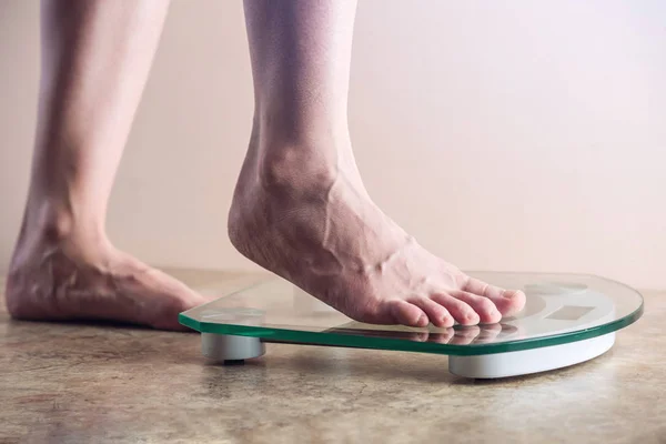Female feet standing on electronic scales for weight control on light background. The concept of sports training, diets and weight loss