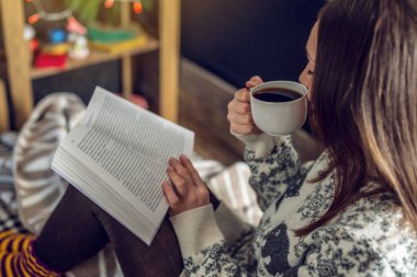 Sıcak bir Noel atmosferinde elinde bir kupa kahveyle kitap okuyan bir kadın. Sıcak yeni yıl havası