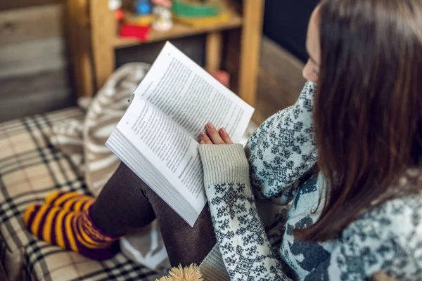 在温暖的圣诞气氛中，穿着毛衣的女人在晚上阅读一本书，喝着一大杯咖啡。 温馨的新年气氛 — 图库照片