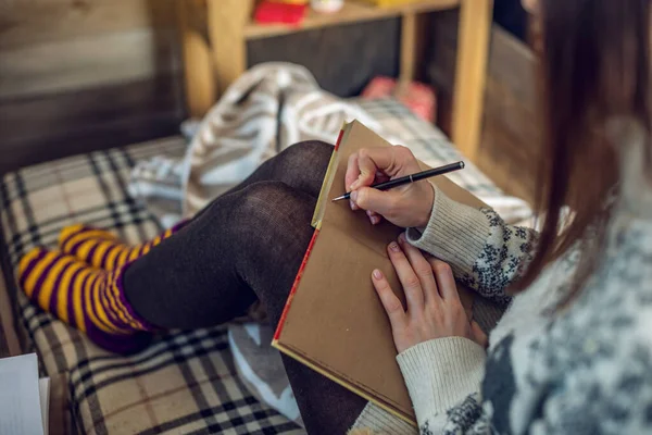 Mujer en un suéter está escribiendo una lista de deseos en un cuaderno en el cálido ambiente de la Navidad. Acogedor estado de ánimo Año Nuevo — Foto de Stock