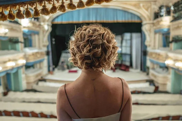 Mulher bonita em um vestido sozinha na varanda de um teatro clássico vazio olha para o palco e interior — Fotografia de Stock