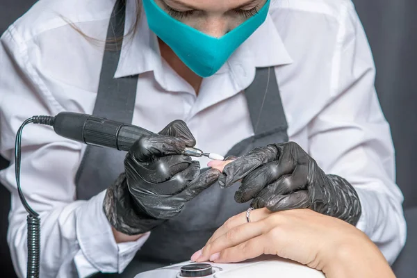 Woman manicure master makes a hardware manicure in black gloves removing the old coating of gel Polish in the salon
