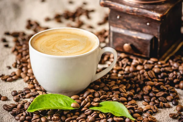 Copa de café con espuma y un molino de café añejo de madera. Bebida fragante y estimulante de frijoles recién tostados. —  Fotos de Stock
