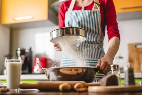 Cocinar ama de casa haciendo galletas en casa en la cocina colorida. Mujer tamiza harina a través del tamiz en la mesa con ingredientes — Foto de Stock