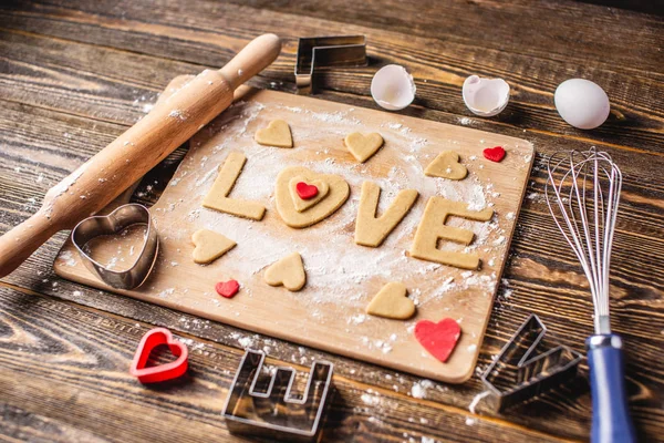 Cozinhar biscoitos da massa em forma de coração e a palavra amor. Cozimento para o dia dos namorados e uma data romântica — Fotografia de Stock