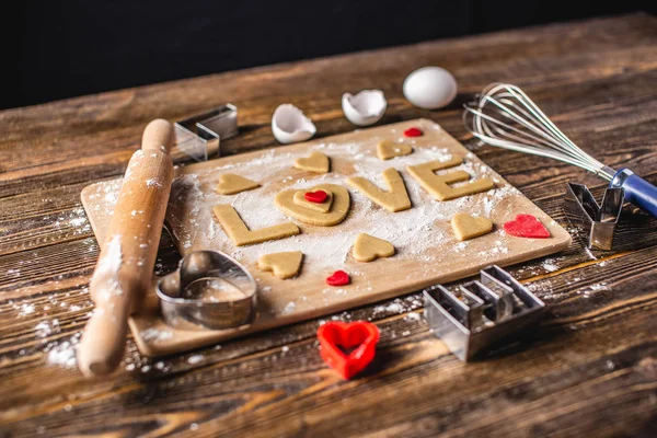 Cozinhar biscoitos da massa em forma de coração e a palavra amor. Cozimento para o dia dos namorados e uma data romântica — Fotografia de Stock