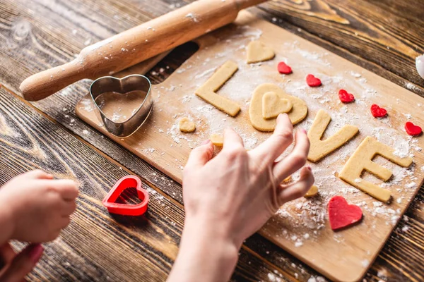 Cozinhar biscoitos da massa em forma de coração e a palavra amor. Cozimento para o dia dos namorados e uma data romântica — Fotografia de Stock