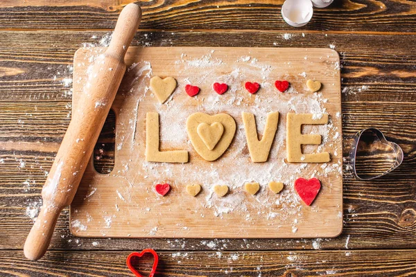 Cozinhar biscoitos da massa em forma de coração e a palavra amor. Cozimento para o dia dos namorados e uma data romântica — Fotografia de Stock