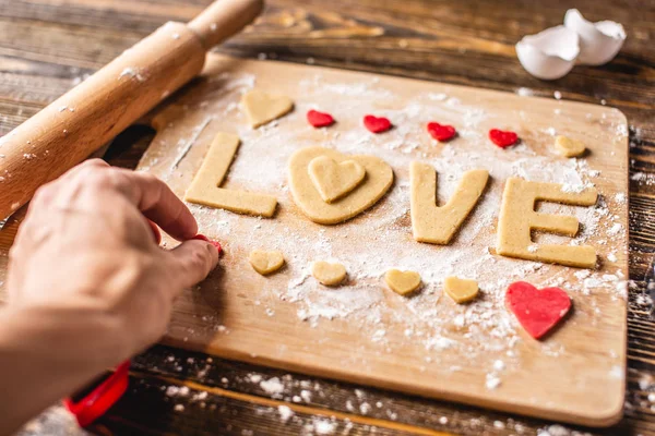 Cozinhar biscoitos da massa em forma de coração e a palavra amor. Cozimento para o dia dos namorados e uma data romântica — Fotografia de Stock