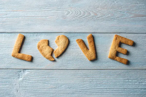 Amor de palavra de um biscoito doce na forma de um coração partido em um fundo de madeira azul. Presente romântico do dia dos namorados — Fotografia de Stock