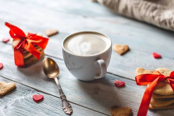 Copo de café e um doce presente de biscoitos amarrados com fita vermelha na forma de corações. Presente romântico do dia dos namorados — Fotografia de Stock