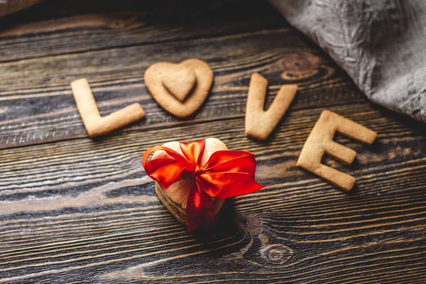 Mensagem de um biscoito doce na forma da palavra amor e um presente amarrado com fita vermelha. Presente romântico do dia dos namorados — Fotografia de Stock