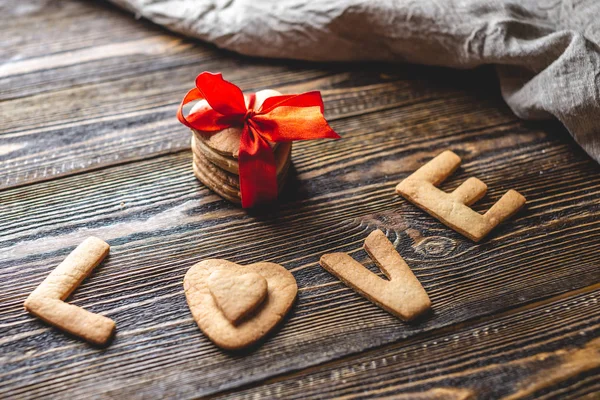 Mensagem de um biscoito doce na forma da palavra amor e um presente amarrado com fita vermelha. Presente romântico do dia dos namorados — Fotografia de Stock