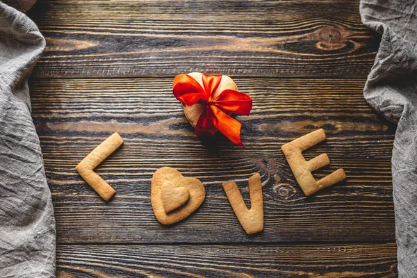 Mensagem de um biscoito doce na forma da palavra amor e um presente amarrado com fita vermelha. Presente romântico do dia dos namorados — Fotografia de Stock