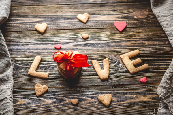 Μήνυμα από ένα γλυκό μπισκότο με τη μορφή της λέξης αγάπη και ένα δώρο δεμένο με κόκκινη κορδέλα. Ρομαντικό δώρο για του Αγίου Βαλεντίνου — Φωτογραφία Αρχείου