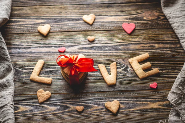 Mensagem de um biscoito doce na forma da palavra amor e um presente amarrado com fita vermelha. Presente romântico do dia dos namorados — Fotografia de Stock