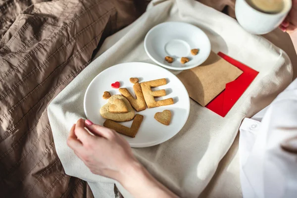 Jovem tem um café da manhã romântico na cama da manhã. Café e amor palavra de biscoitos. Surpresa no dia dos namorados — Fotografia de Stock