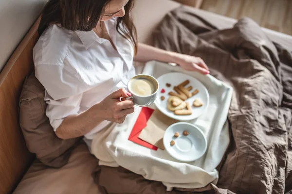 Young woman have a romantic Breakfast in morning bed. Coffee and word love from cookies. Surprise on Valentine's day Stok Foto Bebas Royalti