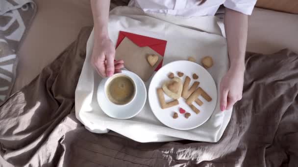 女性は居心地の良い朝のベッドでロマンチックな朝食を持っています。コーヒーとクッキーからの言葉の愛。バレンタインデーの驚き — ストック動画