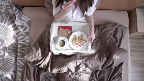 Kobieta ma romantyczne śniadanie w przytulnym porannym łóżku. Kawa i słowo miłość z ciasteczek. Niespodzianka w Walentynki — Wideo stockowe