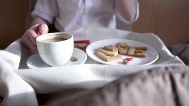 Jonge vrouw heeft een romantisch ontbijt in de ochtend bed. Koffie en woordliefde van koekjes. Verrassing op Valentijnsdag — Stockvideo