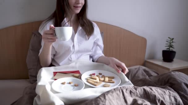 Jonge vrouw heeft een romantisch ontbijt in de ochtend bed. Koffie en woordliefde van koekjes. Verrassing op Valentijnsdag — Stockvideo