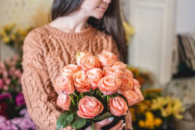 Çiçekçi kadın çiçekçide çiçek açan pembe güllerden büyük bir buket tutuyor.