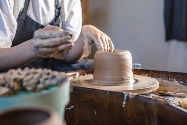 Potter trabajando en una rueda de Potter haciendo un jarrón. Mujer joven formando la arcilla con las manos creando jarra en un taller . — Foto de Stock