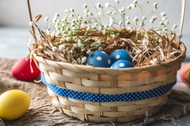 Festive Easter basket with colorful bright eggs and green grass on a wooden table. Traditional spring holiday