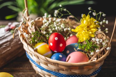 Festive Easter basket with colorful bright eggs and green grass on a wooden table. Traditional spring holiday