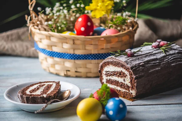 Festive Easter lunch with colorful bright eggs in a basket and an cake on a wooden table. Traditional spring holiday.